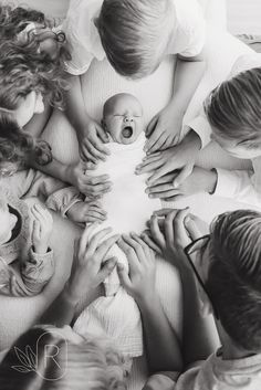 a group of people holding a baby in the middle of a circle with their hands together