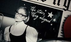 a black and white photo of a woman with glasses in front of a sign that says the stars they aligned