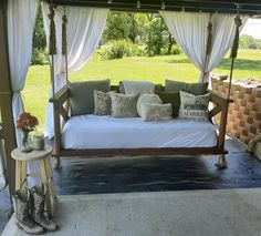 a porch swing bed with white drapes and pillows on the top, in front of a grassy area