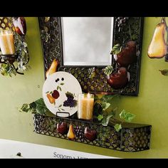 a mirror and some candles on a shelf in a room with green walls, decorated with fruit