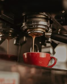 a red coffee cup is being filled with liquid from a coffee maker's espresso machine