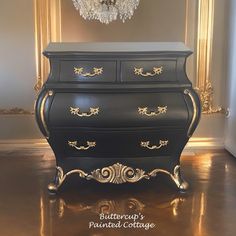 an antique dresser painted black with gold trim and ornate details on the top, in front of a chandelier