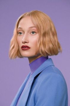 a woman with blonde hair wearing a blue jacket and purple shirt, looking at the camera