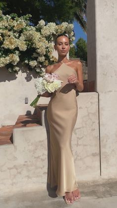 a woman in a long dress holding flowers and posing for the camera with her hand on her hip