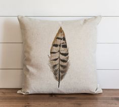 a pillow with a feather on it sitting on top of a wooden floor next to a white wall