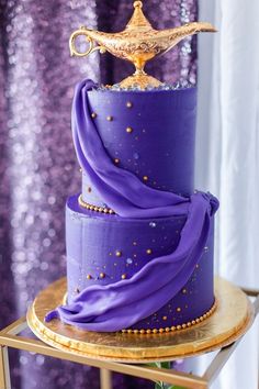 a purple cake with gold decorations on the top and bottom is sitting on a table