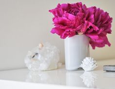 a white vase filled with pink flowers sitting on top of a table next to a pair of scissors