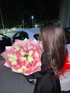 a woman holding a bouquet of roses in front of her car at night with the tail light on