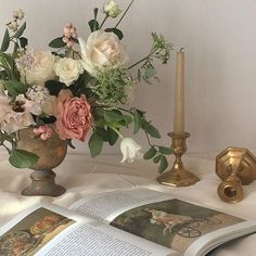 an open book on a table next to a vase with flowers and candlesticks