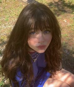 a woman with long brown hair and blue shirt sitting on the ground next to a tree