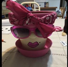 a pink hat and sunglasses on top of a bowl with a face painted on it