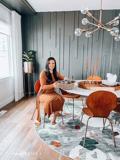 a woman sitting at a round table in front of a chandelier with hanging lights