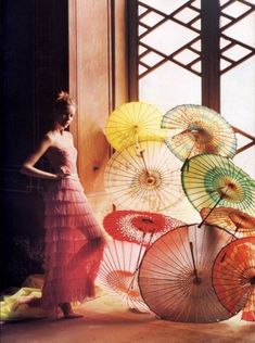 a woman standing in front of an open window holding colorful umbrellas