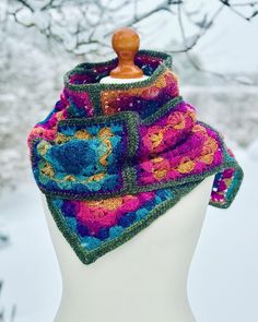 a white mannequin wearing a multicolored crocheted scarf on top of it