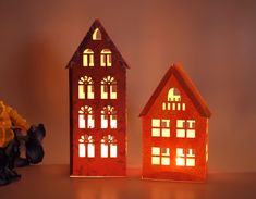 two paper houses sitting next to each other on top of a table with flowers in front of them