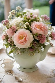 a tea pot filled with lots of flowers on top of a white tablecloth covered table