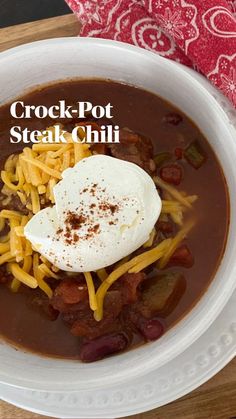 a white bowl filled with chili, beans and sour cream on top of a wooden cutting board