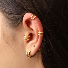 a woman wearing gold ear cuffs and piercings on her left ear, with two small rings in the middle