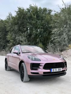 a pink porsche cayen is parked in front of some trees