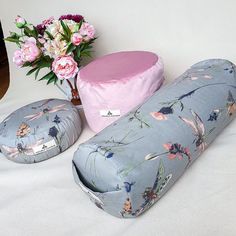 three pillows and a vase with flowers on a white tableclothed surface next to each other