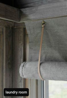 a gray curtain hanging from the side of a window with a leather handle on it