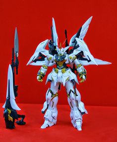 a white and black robot standing next to a red wall with two knives in it's hands