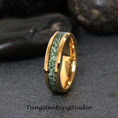 a gold ring with green moss inlays on the outside and inside, sitting next to some rocks