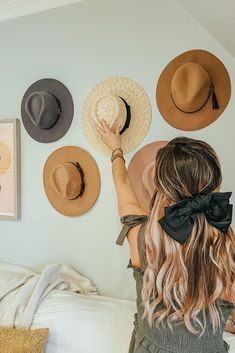 a woman with her hands on the wall and four hats hanging above her head,