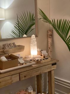 a wooden table topped with lots of items next to a mirror and palm leaf lamp