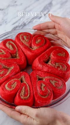 red velvet cinnamon rolls in a glass bowl on a marble countertop with two hands reaching for one