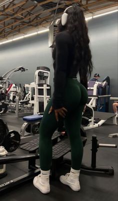 a woman in green leggings and headphones is sitting on a gym machine