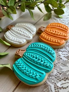 three decorated cookies sitting on top of a wooden table next to green leaves and flowers