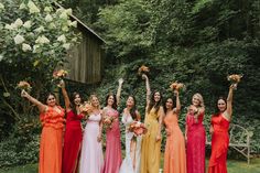 a group of women standing next to each other holding flowers in front of trees and bushes