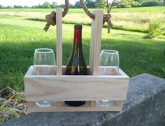 two wine glasses and a bottle in a wooden crate with rope handles on the grass