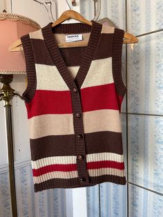 "This classic vest is made of 50 per cent Shetland wool and 50 per cent acrylic in light beige, tan, dark brown and red stripes. It has the original brown turtle buttons in the front. The label reads \"Pandora Scotchkin.\" The measurements, taken with the vest lying flat, are: shoulder to shoulder, 13 1/2 inches; armpit to armpit, 16 inches; length, 23 inches; bottom edge, 16 inches (with stretchy ribbing). The vest overall has some stretch. In very good condition." Red Wool Vest For Winter, Classic Brown Wool Sweater Vest, Classic Beige Wool Sweater Vest, Vintage Brown Sweater Vest For Fall, Brown Wool Vest For Winter, Retro Brown Sweater Vest For Winter, Classic Brown Sweater Vest For Fall, Striped Sleeveless Sweater Vest For Fall, Brown Wool Vest For Fall