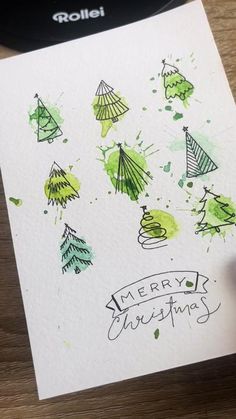 someone is holding up a christmas card that has trees on it and the words merry festing written in green ink