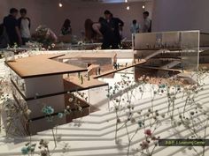 people are looking at model houses on display in an art gallery with flowers growing out of them