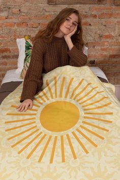 a woman sitting on top of a bed next to a yellow sun print comforter