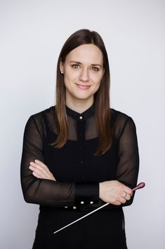 a woman standing with her arms crossed and looking at the camera while wearing a black dress