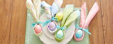 an arrangement of decorated easter eggs on a plate with ribbons and napkins tied around them