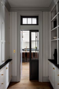 an open door leading to a kitchen with white cabinets and black counter tops on either side