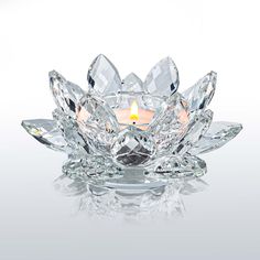 a crystal flower candle holder with a lit candle in the center on a reflective surface