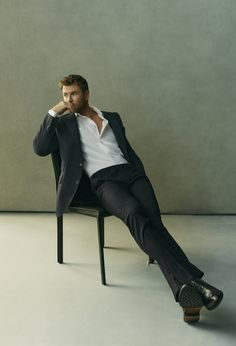 a man in a suit sitting on a chair with his legs crossed and hands behind his head