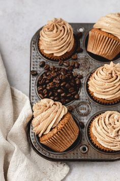 cupcakes with frosting in a muffin tin on a table next to coffee beans