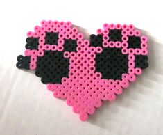 a pink and black heart shaped beaded brooch on a white surface with the word love spelled in it