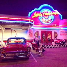 an old car is parked in front of a diner with neon signs on the building