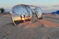 two people are reflected in the mirrored sunglasses on the sand at sunset or sunrise,