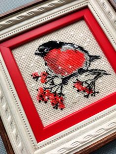 a red and black bird sitting on top of a white framed artwork with cherry blossoms