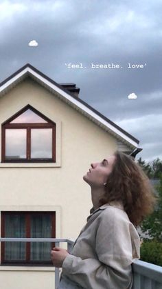 a woman standing in front of a house looking up at the sky with her eyes closed