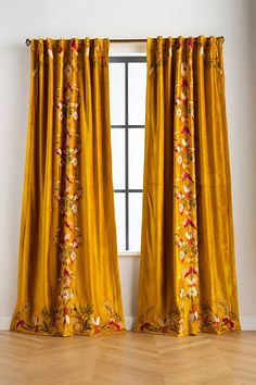 a yellow curtain with flowers on it is in front of a white wall and hardwood floor